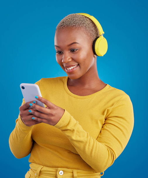 Happy, phone and music with black woman in studio for streaming, multimedia and browsing. Search, smile and audio with female and headphones on blue background for listening, online radio and songs. - Foto, Imagem