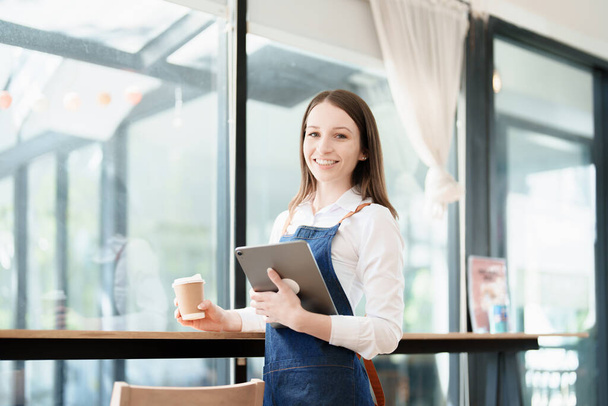 Starting and opening a small business, a young Asian woman showing a smiling face in an apron standing in front of a coffee shop bar counter. Business Owner, Restaurant, Barista, Cafe, Online SME. - Foto, imagen