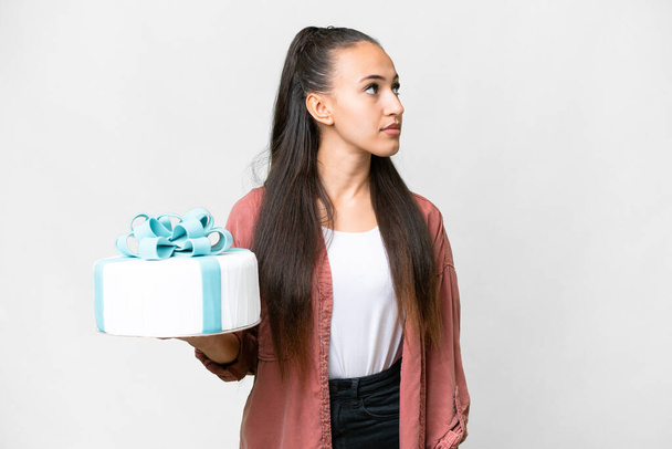Young Arabian woman holding birthday cake over isolated white background looking to the side - Photo, Image