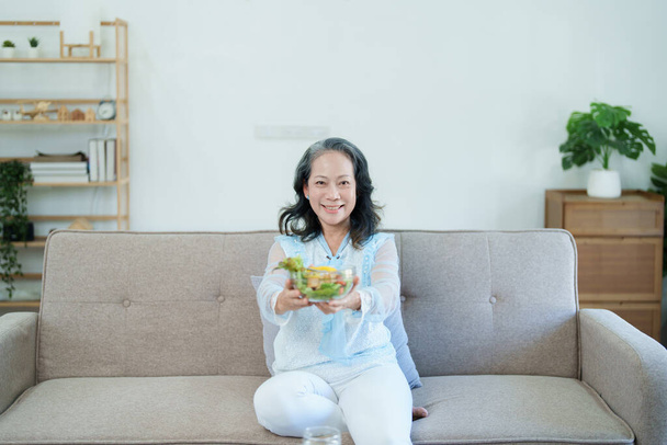 Портрет пожилой азиатки, которая заботится о своем здоровье, поедая салат - Фото, изображение
