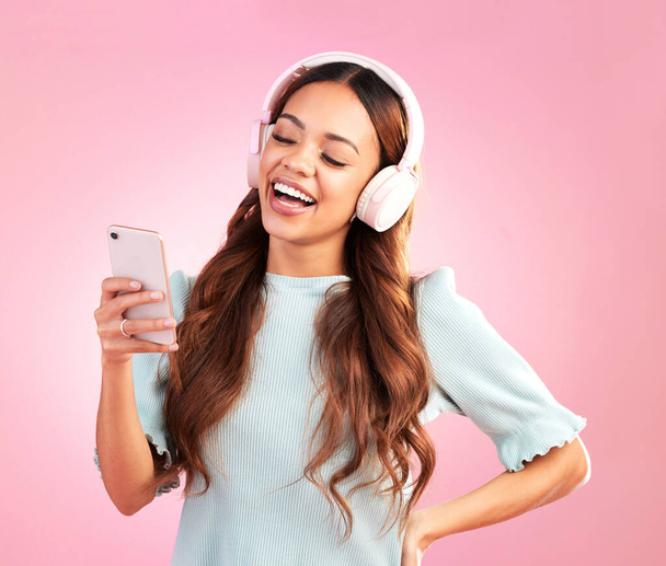 Phone, music headphones and woman singing in studio isolated on a pink background. Cellphone, radio singer and happy female with mobile streaming, laughing and listening to audio, sound or podcast - Foto, imagen