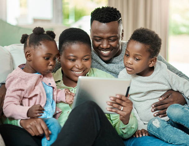 Trávit nějaký rodinný čas online. láskyplná mladá čtyřčlenná rodina, která používá tablet, zatímco sedí na pohovce v obývacím pokoji doma - Fotografie, Obrázek