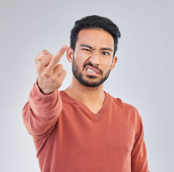 Rude, middle finger and portrait of asian man in studio for fail, conflict and problem. Annoyed, upset and aggressive with male and hand gesture on gray background for hate, disrespect and furious. - Foto, Imagen