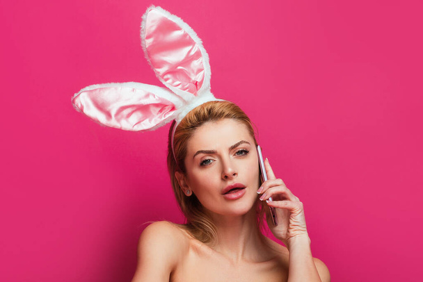 Easter woman with rabbit ears talking on phone, isolated on pink - Photo, image