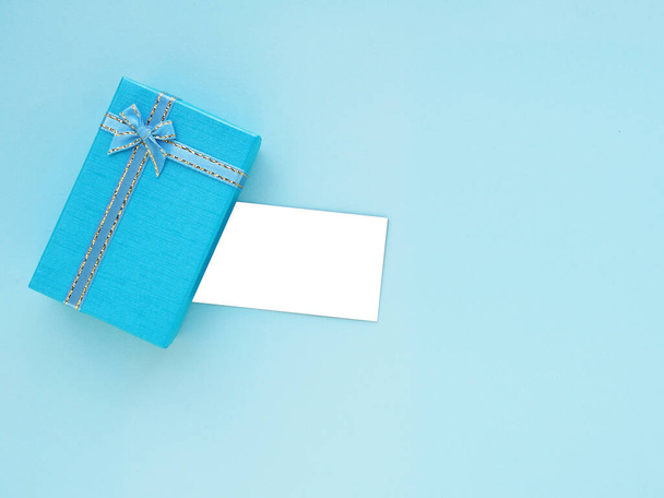 Caixa de presente azul com arco e cartão branco vazio no fundo azul. Vista superior, flat lay com espaço de cópia. Conceito de fundo festivo - Foto, Imagem