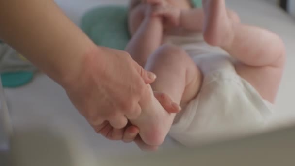 Close-up shot van zorgzame moeder aanraken of doen massage pasgeboren benen. Kleine blanke baby in luier liggend op laken in witte wieg. Begrip ouderschap, zorgeloze kindertijd, gezin en liefde. - Video