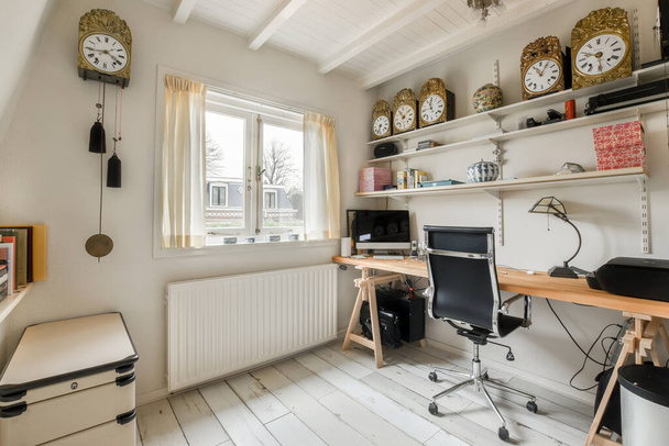 a home office with clocks on the wall and desk in front of window looking out onto an outside view - Photo, Image