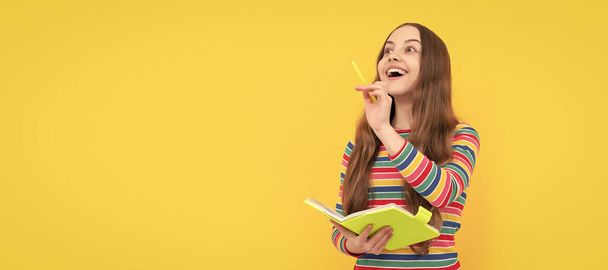 Happy kid genius got inspiration holding book and pointing pen up yellow background, idea. Banner of schoolgirl student. School child pupil portrait with copy space - Photo, image