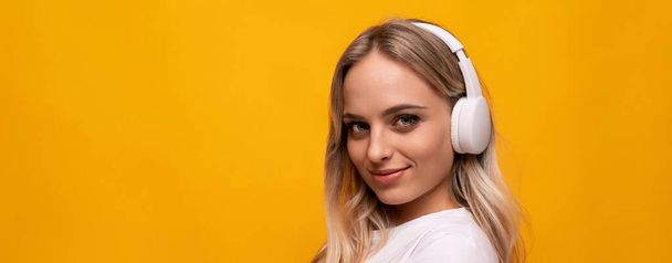 glimlachende vrouw luisteren naar muziek in witte koptelefoon op oranje achtergrond met lege ruimte. - Foto, afbeelding