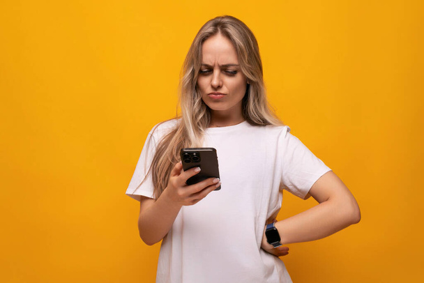 Девушка в неверии держит телефон в руках на желтом фоне. - Фото, изображение