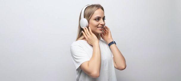 horizontale foto van een jonge vrouw in een witte tank top luisteren naar een podcast in draadloze hoofdtelefoon op een witte achtergrond met vrije ruimte. - Foto, afbeelding