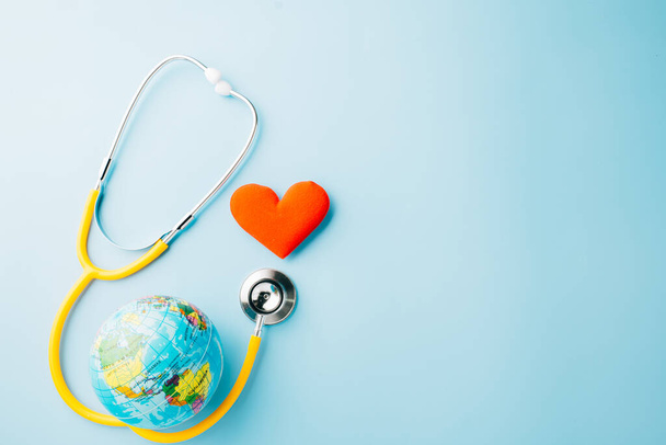 World Health Day. Yellow doctor stethoscope and world globe with Red heart shape isolated on blue background with copy space, Save world day, Green Earth Environment, Healthcare and medical concept - Valokuva, kuva