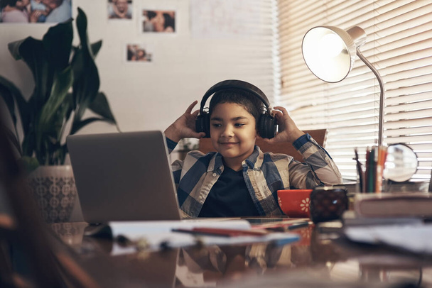 Klasa jest bliżej niż ci się wydaje. uroczy chłopiec korzystający z laptopa i słuchawek podczas wykonywania zadania szkolnego w domu - Zdjęcie, obraz