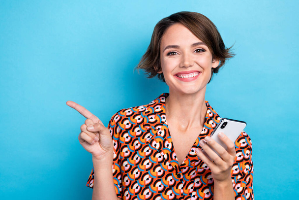 Portrait of cheerful gorgeous girl toothy smile hold smart phone direct finger empty space isolated on blue color background. - Foto, Bild
