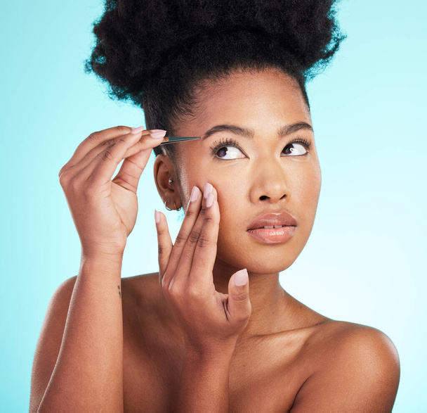 Beauty, hair removal and eyebrows with black woman and tweezer in studio for cosmetics, grooming and self care. Spa, growth and aesthetic with model on blue background for natural, fresh and shaping. - Φωτογραφία, εικόνα