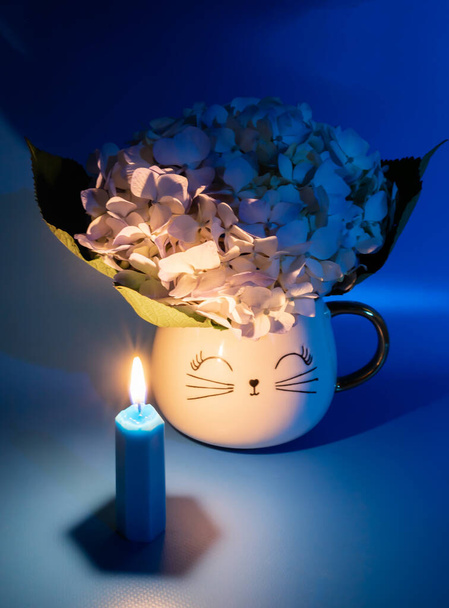 Asetelma hortensia kukka kuppi ja polttava kynttilä sininen väri - Valokuva, kuva