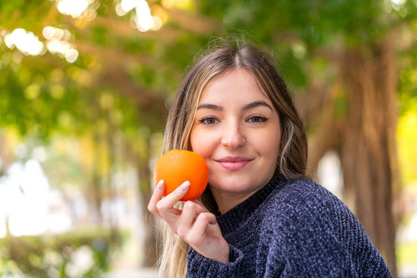 Young pretty Romanian woman holding an orange at outdoors - Фото, зображення