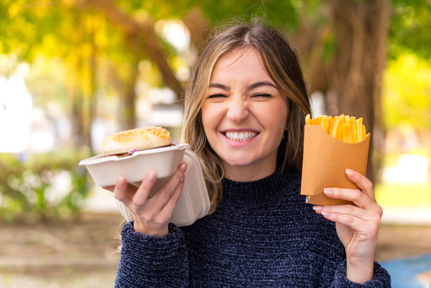 Jonge mooie Roemeense vrouw met hamburger en chips in de buitenlucht - Foto, afbeelding