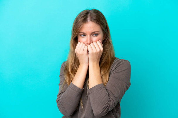 Young blonde woman isolated on blue background nervous and scared putting hands to mouth - Foto, Imagem