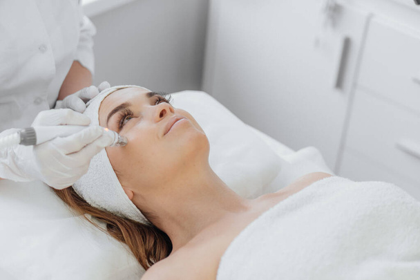 Radiofrequency facial skin lifting. Hardware cosmetology RF lifting procedure and hardware facial massage. Rejuvenation, skin care in a beauty salon. Woman doctor cosmetologist and girl in spa clinic. - Fotografie, Obrázek