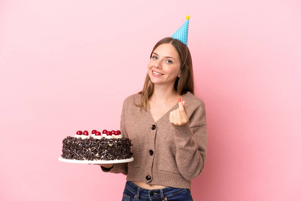 若いですリトアニア女性保持誕生日ケーキ隔離上のピンクの背景作るお金ジェスチャー - 写真・画像