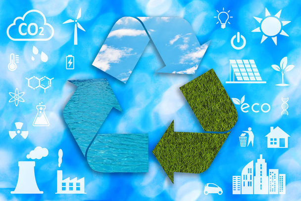 Um grande símbolo de reciclagem texturizado com água, céu azul e grama verde e outros ícones de ecologia branca no fundo desfocado. - Foto, Imagem
