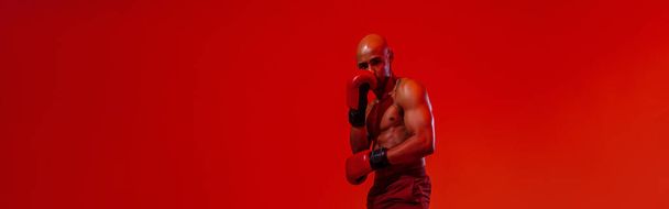 Man wearing boxing gloves practicing for fight on studio background with color filter - Photo, image