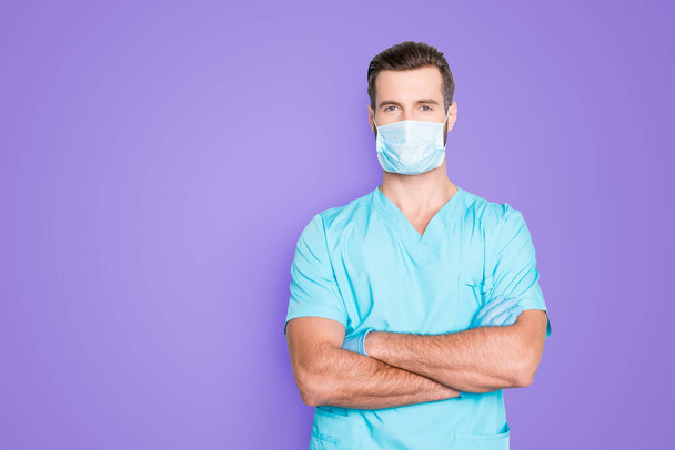 Portrait with copyspace, empty place of attractive handsome man in sterile mask and blue lab uniform, having his arms crossed, looking at camera isolated on grey background. - Fotografie, Obrázek