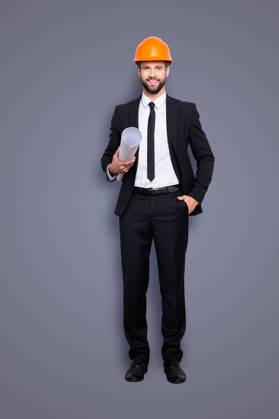 Full length size portrait of attractive cheerful joyful investor in orange hard hat and black tux, tuxedo with tie, looking at camera, isolated on grey background, having paper roll in hand. - Φωτογραφία, εικόνα