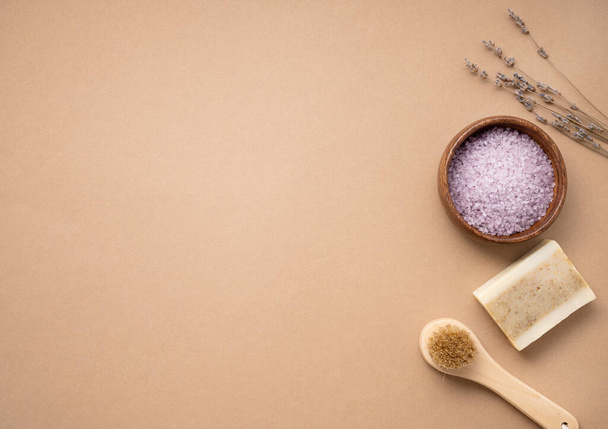 Flat lay organic sea salt for the body with dry lavender flowers, brush and soap  on a beige background. Skin care. The concept of a natural and eco-friendly spa product. Top view, copy space. - Photo, image