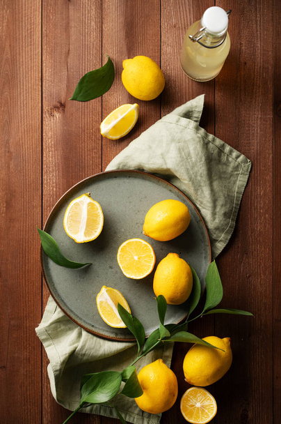 緑のプレートに葉が入った新鮮なレモンと、暗い木製の背景にレモンドリンクのボトル。新鮮な絞りレモネードのための柑橘類。暗い組成と素朴なスタイル。トップ表示. - 写真・画像