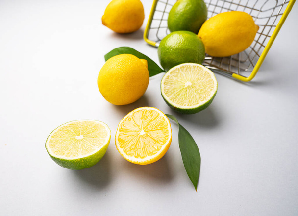 Fresh lemons and limes fall out of  a supermarket basket on a blue background. Citrus fruit concept for freshly squeezed lemonade.  - 写真・画像
