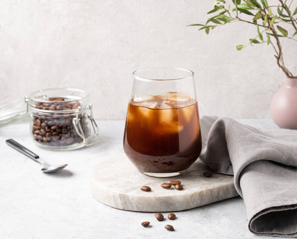 Eiskaffee in einem Glas mit Eiswürfeln und Körnern auf hellem Marmorhintergrund. Das Konzept eines kalten Sommergetränks. - Foto, Bild