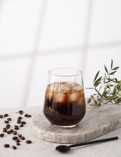 IJskoffie in een glas met ijsblokjes en korrels op een lichte marmeren achtergrond met ochtendschaduwen. Het concept van een koud zomerdrankje. Kopieerruimte. - Foto, afbeelding