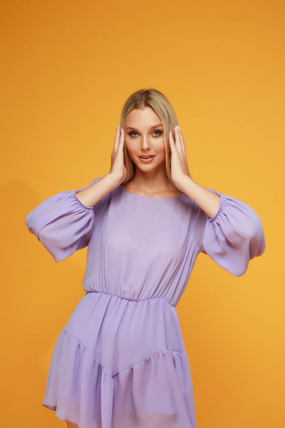 Beautiful blonde girl in a lilac dress on a yellow background. Studio. Smile and emotions. - Photo, image