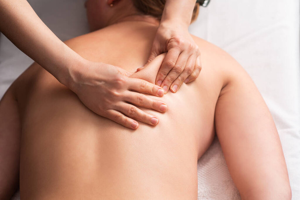 白い背景のマッサージテーブルの上に若い女性のマッサージの背中と肩の刃。マッサージスパの治療の概念。体を弛緩させる。閉鎖 - 写真・画像