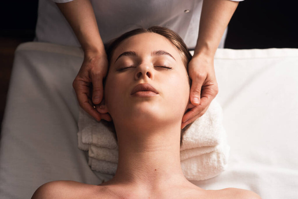 masseur doing facial massage to young woman on massage table on white background. Concept of massage spa treatments. Close-up - Φωτογραφία, εικόνα