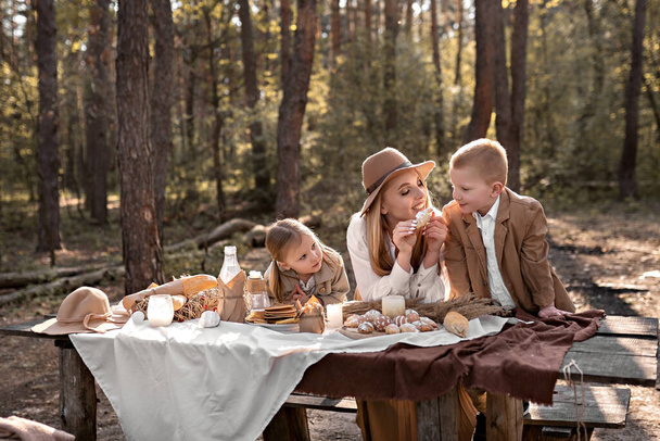 Happy family with children having fun and celebrating Easter in the spring forest on a picnic. A pregnant mother feeds her son with a croissant. Table decor - pancakes, eggs in a rustic style - Photo, Image