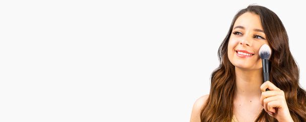 Bannière avec jeune femme souriante heureuse appliquant contouring ou blush sur les joues avec une grande brosse. - Photo, image