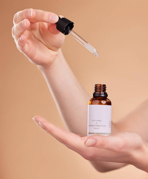 Hands, serum bottle and pipette for skincare in studio isolated on a brown background. Dermatology product, cosmetics and woman or model with hyaluronic acid, retinol or essential oil for anti aging - 写真・画像