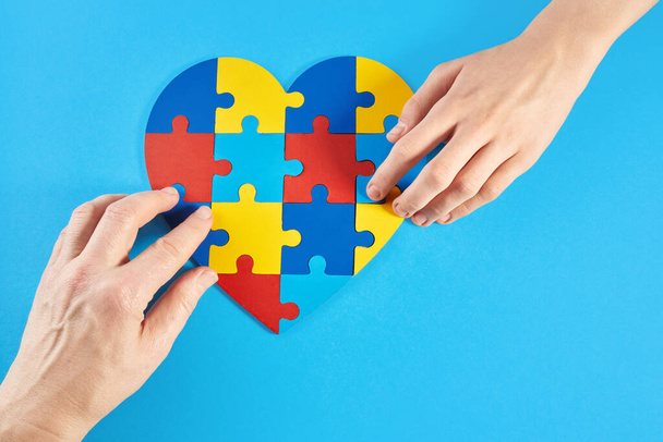 Father and autistic son hands holding jigsaw puzzle heart shape. Autism spectrum disorder family support concept. World Autism Awareness Day. - Photo, Image