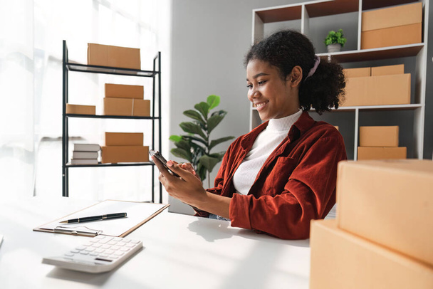 Sme business idee. Afro-Amerikanen vrouw online verkopen thuis met laptop om bestellingen aan te nemen en om gele pakket dozen online levering ideeën te leveren. - Foto, afbeelding