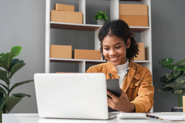 sme business idea. African Americans woman selling online at home with laptop to take orders and to deliver yellow parcel boxes online delivery ideas. - Foto, Imagem