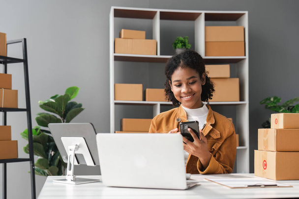 Sme business idee. Afro-Amerikanen vrouw online verkopen thuis met laptop om bestellingen aan te nemen en om gele pakket dozen online levering ideeën te leveren. - Foto, afbeelding