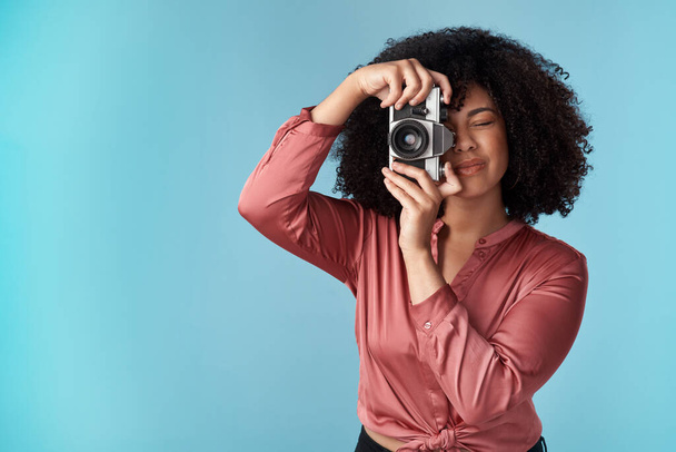 Stúdiófelvétel egy fiatal nőről, aki kamerát használ kék háttérrel. - Fotó, kép
