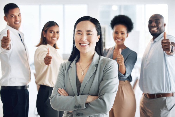 Asian woman, leadership and arms crossed, team and thumbs up, lead and professional mindset with collaboration. Diversity, teamwork and agreement, corporate group in workplace and smile in portrait. - Valokuva, kuva