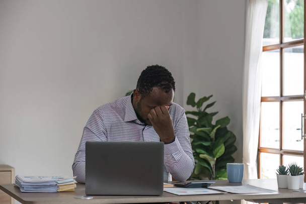 Uomo d'affari stressato seduto sul posto di lavoro dell'ufficio. Uomo nero stanco e oberato di lavoro. Giovani afro-americani esausti uomini sotto stress che lavorano sul computer portatile. - Foto, immagini