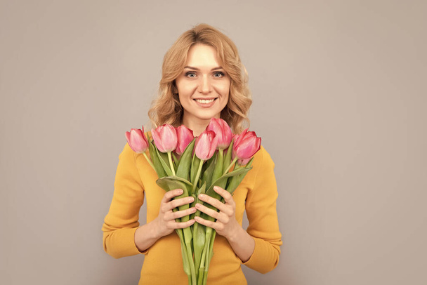 onnellinen nainen pidä kukkia kevään loma harmaalla pohjalla. - Valokuva, kuva