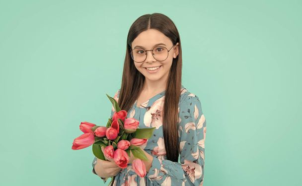 母や女の日。子供は3月8日に花を持ってる。青い背景に春の花束を持つ10代の女の子。花のプレゼント。チューリップ付きのメガネの幸せな子供. - 写真・画像