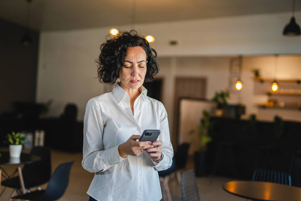 Uma mulher madura usar smartphone em casa ou no trabalho frustrado louco - Foto, Imagem